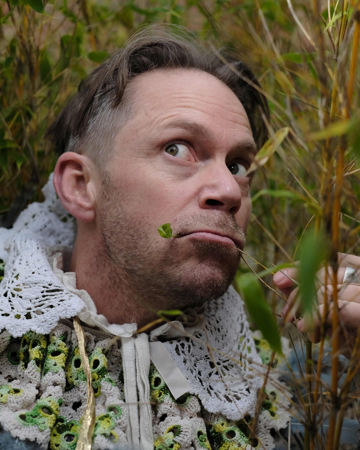En medtsåmmårnattsdrøm, skuespiller i kostyme med krage av kniplinger, liggende i høyt gress med et blad i munnen
